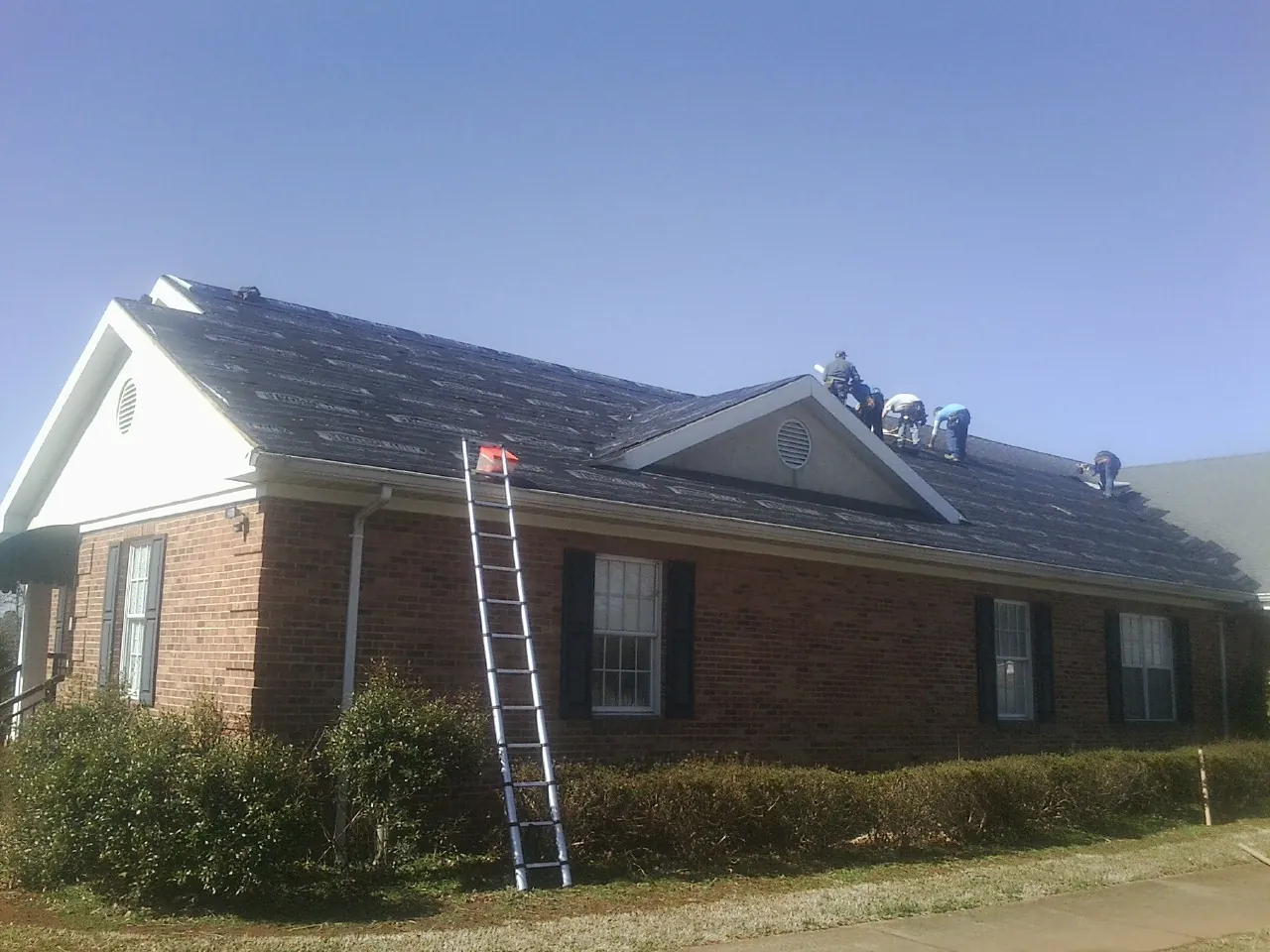Crew tearing shingles off a brick ranch roof with a ladder set — Metal Roof Repair work by our crew in Ellabell