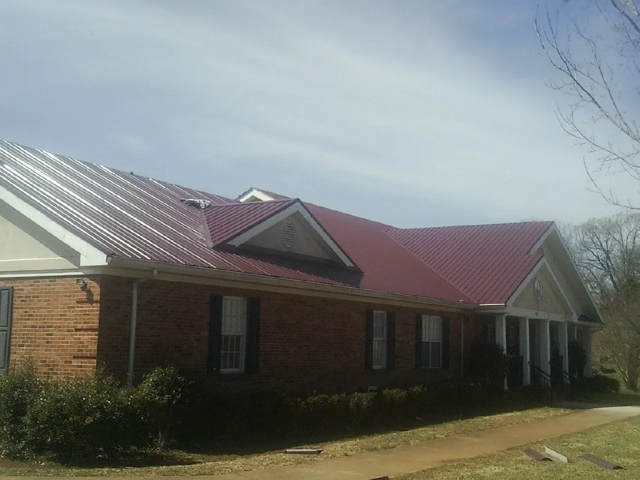Red metal roof with gabled entries on a long brick building, from a Hail Damage Roof Repair job in Ellabell