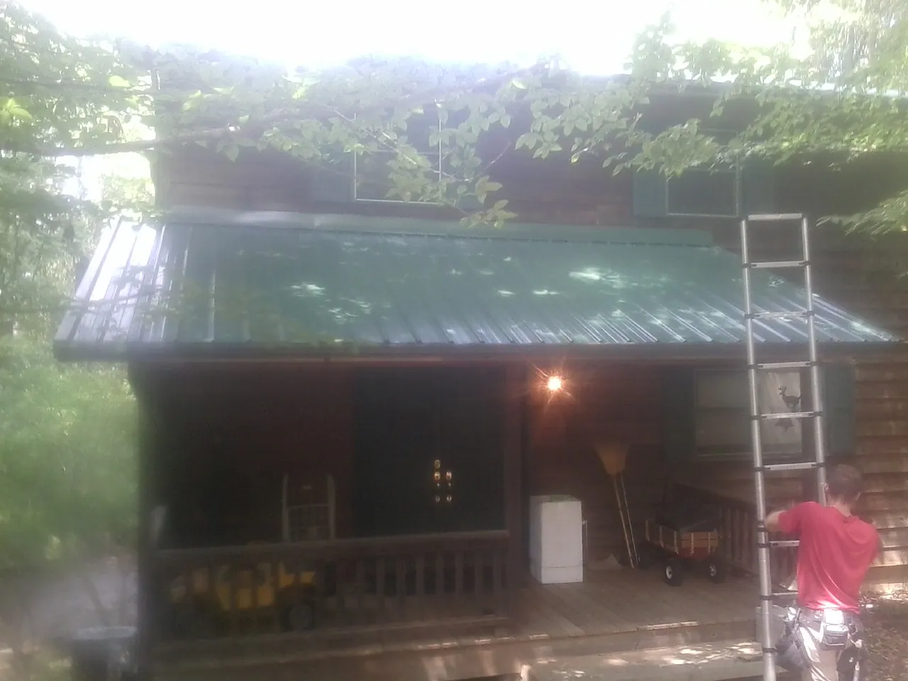 Worker on a ladder at the green porch roof of a wooded cabin in Ellabell
