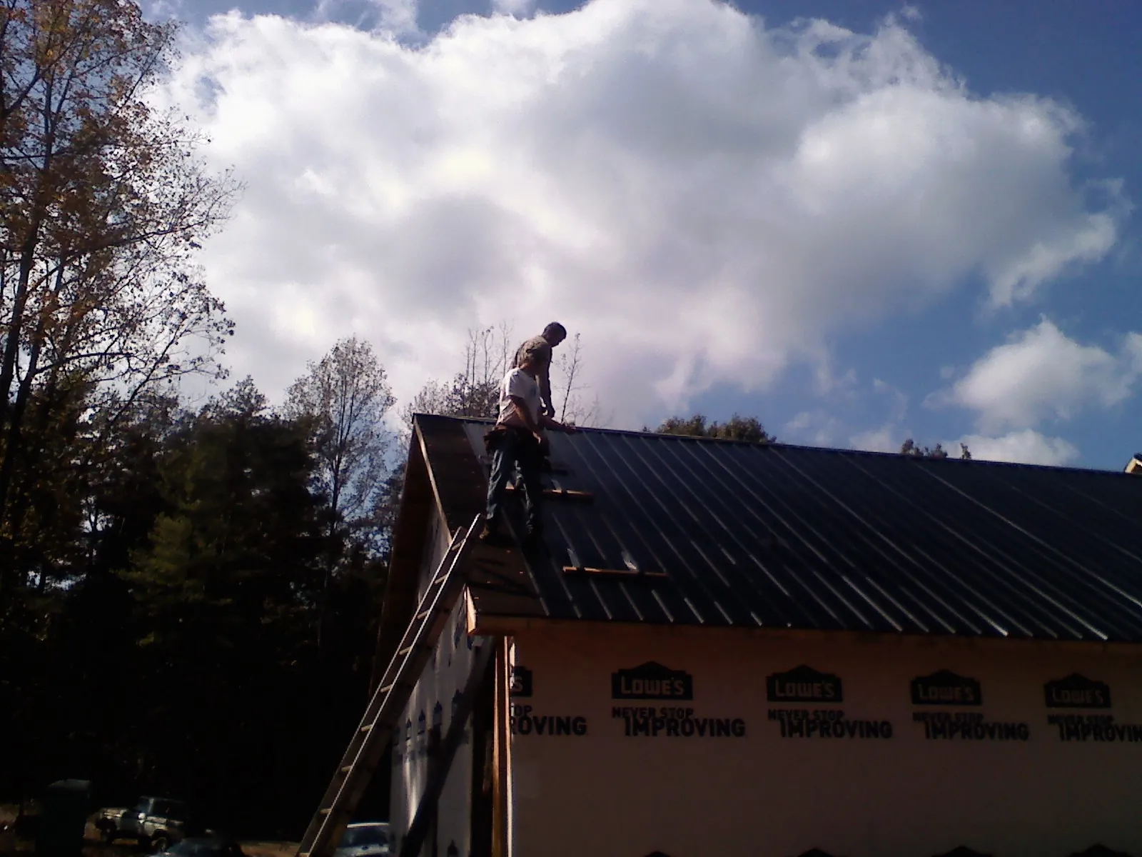 Roofer fastening dark metal panels high against a cloudy sky, from a Roof Inspection job in Ellabell