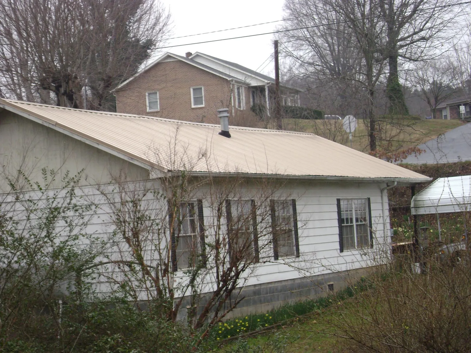 Tan metal roof on a white sided house set into a hillside — Commercial Roofing by Roofing Brothers in Ellabell