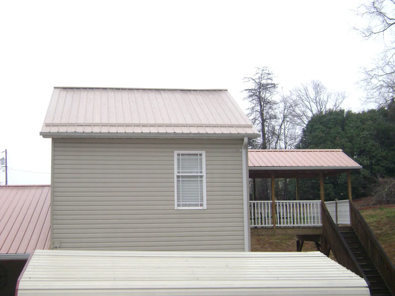 Tan metal roofs on a two story addition and attached porch, from a Roof Replacement job in Ellabell